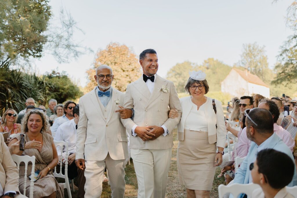 Arrivé du marié au bras de ses parents lors de la cérémonie laique au Domaine de la Fauconnie en Dordogne par la photographe de mariage Jade Sequeval